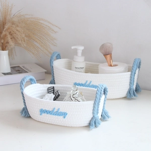 Detail of two white woven storage baskets with blue tassels and goodday embroidery