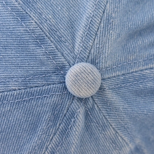 Close-up detail of reinforced top button and stitching on washed blue denim baseball cap
