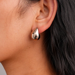 Close-up of a minimalist gold teardrop earring with a polished mirror finish on model