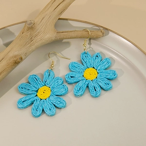 Détail de boucles d'oreilles marguerites tissées bleu et jaune sur support en bois