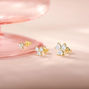 Detailed macro shot of clover-shaped gold earrings with heart-cut clear cubic zirconia
