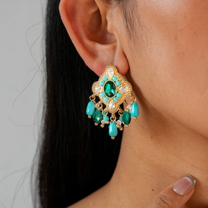 Detailed macro view of vintage gold earrings with emerald crystal and turquoise beads