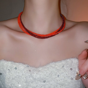 Detail of multilayer red seed bead necklace styled with a white sequin top