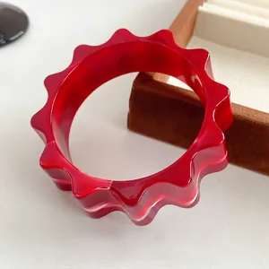 Fashionable red resin bangle featuring unique wavy texture and translucent finish