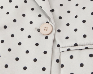 Détail macro du blazer en satin gris clair à pois noirs avec un bouton en résine