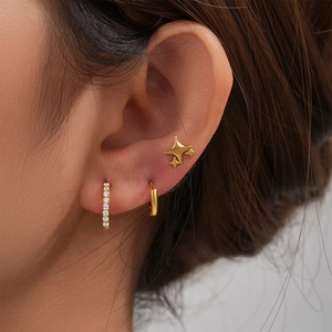 Detail view of 925 silver star studs and gold hoop earrings set on a model's ear