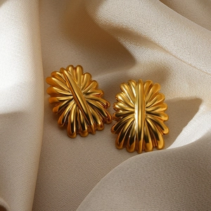 Detailed close-up of golden radial textured floral earrings on champagne silk background