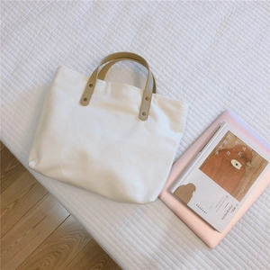 Close-up of beige canvas tote with brown leather handles and copper rivet details