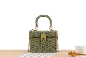 Detail of green woven straw box bag with leather strap and gold metal clasp on table