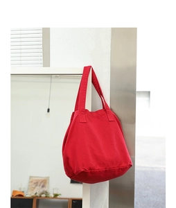 Minimalist red washed canvas tote bag hanging on a bright indoor white wall corner