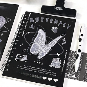 Close-up of black spiral notebook featuring a glass butterfly design and stationery props
