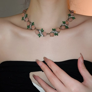 Detailed close-up of a vintage floral necklace with pink oval gems and green leaf elements