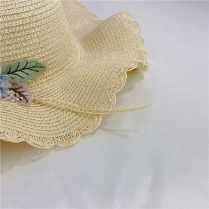 Close-up of beige straw hat featuring delicate leaf embroidery and wavy openwork brim