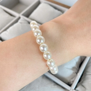 Classic white pearl bracelet with gold beads worn on wrist over jewelry tray