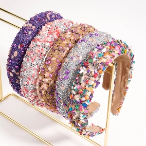 Baroque headbands with colorful gemstones displayed on a gold metal stand with white background
