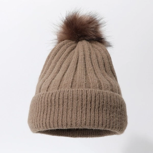 Detail of dark brown chunky knit beanie featuring a fluffy matching faux fur pom-pom