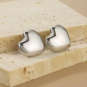 Close-up of glossy silver 3D hollow heart stud earrings on a stone textured surface
