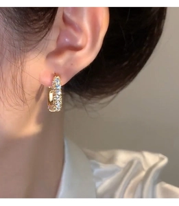 Close-up of gold zircon square hoop earring worn by model with shimmering stone inlay