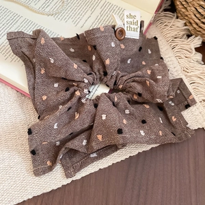 Detail of coffee polka dot scrunchie with wooden button and woven label on a book