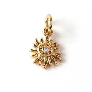 Macro view of gold-plated sunburst charm pendant with sparkling cubic zirconia inlay
