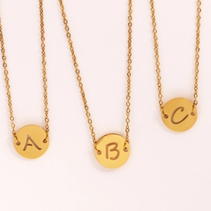 Détail de trois colliers en acier doré avec pendentifs ronds gravés des lettres A B C