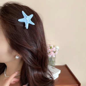 Detail of matte blue starfish hair clip worn by a model in a coastal vacation style