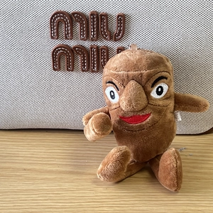 Brown shark plush keychain with red lips and big nose detail on woven bag background