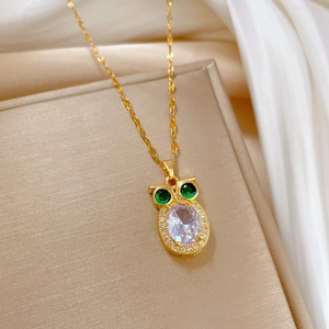 Close-up of golden owl pendant with large oval gemstone and green crystal eyes