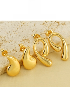 Detail of 18K gold plated teardrop and twisted hoop earrings on textured stone surface