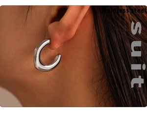 Close-up of a silver-tone chunky C-shaped stainless steel earring worn on the earlobe