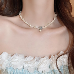Detail view of pearl necklace featuring a square pendant and drop pearl on model neck