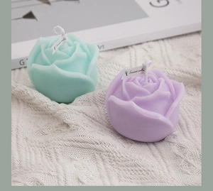 Top view of rose shaped scented candles in mint green and purple on a white knit background