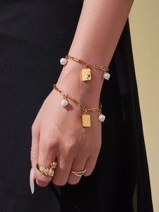 Detailed shot of golden link bracelet with pearl charms and a rectangular pendant on wrist