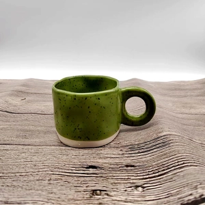 Minimalist green speckled ceramic mug with round handle on a wavy light wood surface