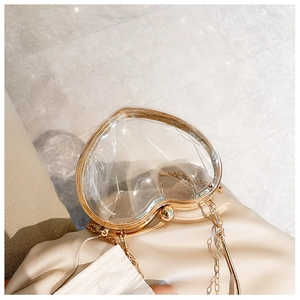 Macro shot of a transparent heart-shaped acrylic clutch with gold metal frame and chain strap