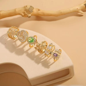 Detail of luxury 14K gold plated rings with green zircon and geometric textures on ceramic