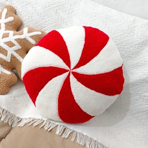 Close-up of a plush peppermint candy pillow on a white knitted blanket with fringe