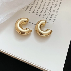 Detailed close-up of polished gold C-shape hoop earrings on minimalist book prop