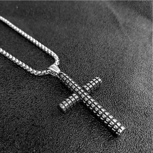 Macro detail of silver stainless steel cross pendant with grid texture and box chain