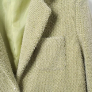 Close-up van lichtgroene suède blazer met zachte textuur en zakafwerking