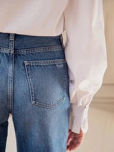 Detail of white ruffle cuff sleeve paired with blue denim jeans featuring ROSAE embroidery