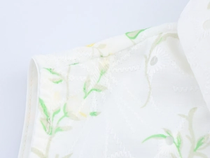 Dettaglio macro del tessuto bianco con stampa floreale verde e ricamo traforato