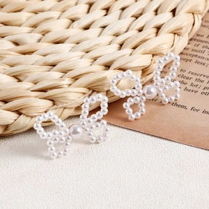 Macro shot of handmade pearl bow earrings on vintage paper and woven background