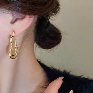 Close-up of golden wavy hoop earrings worn by a model showcasing polished fluid design