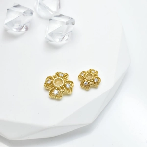 Golden flower-shaped jewelry charms with white zircon inlay on white marble stand