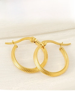 Close-up of golden stainless steel hoop earrings with textured diagonal stripe engraving