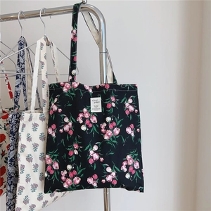 Close-up of black floral canvas tote bag with pink tulip pattern and white logo tag