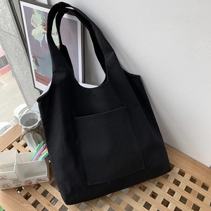 Detail of a black canvas tote bag with front pocket placed on a wooden bench