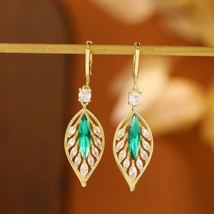 Detailed close-up of leaf-shaped gold earrings with green marquise stones on a display stand