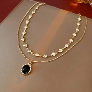 Close-up of double-layered gold heart necklace with vintage black oval gemstone pendant